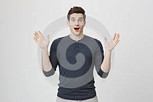 Portrait of good-looking male model expressing surprise and joy raising his hands, isolated over white background. Man