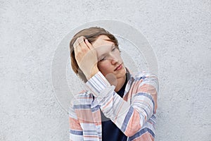 Portrait of good-looking male with trendy hairstyle holding his hand on hair looking aside with dreamy expression. Teenage boy pos