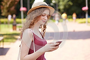 Portrait of good looking positive girl being in good mood typing messages to her friends having walk in recreation zone, holding