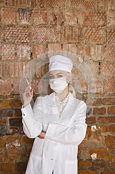 Portrait of a good looking young blond nurse with disposable syringe in her arms in a red brick background.