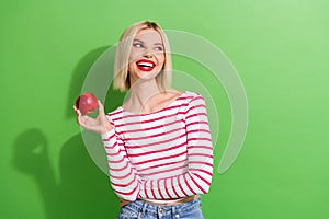 Portrait of good mood gorgeous girl dressed striped clothes hold apple look at offer empty space isolated on green color
