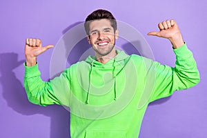 Portrait of good mood nice self confident guy with brunet hairdo green hoodie directing at himself isolated on violet