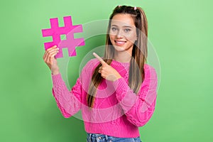 Portrait of good mood positive girl with straight hairstyle wear knit pullover indicating at hashtag isolated on green