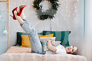 Portrait of gorgeous brunette woman in red high heels is having fun in bed and posing in the Christmas decorated interior