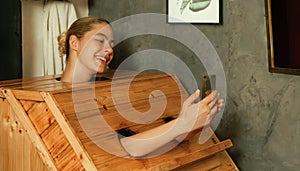 Gorgeous woman playing her mobile phone while using sauna cabinet.Tranquility