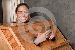 Gorgeous woman playing her mobile phone while using sauna cabinet.Tranquility