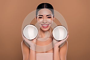 Portrait of gorgeous lady holding two coconuts enjoying vitamins procedure for skin isolated on beige color background