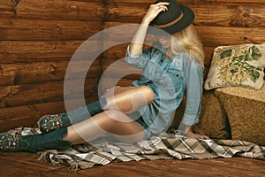 Portrait of gorgeous long-legged girl wearing jeans shorts, shirt, suede boots with floral embroidery and stetson felt hat