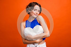 Portrait of gorgeous lovely girl closed eyes arms hold soft comfy heart cushion isolated on orange color background