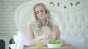 Portrait of gorgeous pregnant woman drinking orange juice and eating green grapes at home. Happy Caucasian beautiful