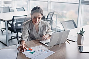 Portrait of gorgeous, smiling young female studying charts at her workplace