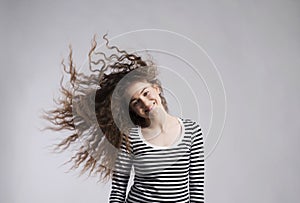 Portrait of a gorgeous teenage girl with curly hair, blowing in wind. Studio shot, white background with copy space