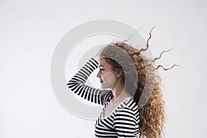 Portrait of a gorgeous teenage girl with curly hair, blowing in wind. Studio shot, white background with copy space