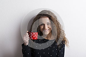 Portrait of a gorgeous teenage girl with curly hair drinking tea from mug. Studio shot, white background with copy space