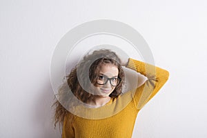 Portrait of a gorgeous teenage girl with curly hair and eyeglasses. Studio shot, white background with copy space