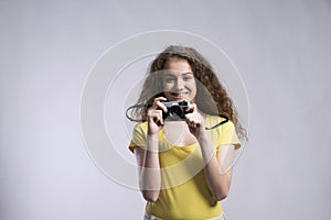 Portrait of a gorgeous teenage girl with curly hair holding camera. Studio shot, white background with copy space