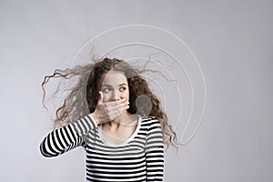 Portrait of a gorgeous teenage girl with curly hair,holding hand in front of mouth. Studio shot, white background with