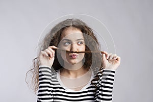 Portrait of a gorgeous teenage girl with curly hair, holding lock of hair as a moustache. Studio shot, white background