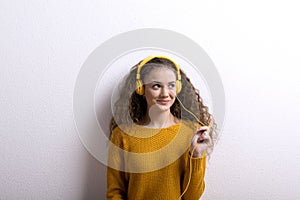 Portrait of a gorgeous teenage girl with curly hair, listening music via headphones. Studio shot, white background with