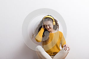 Portrait of a gorgeous teenage girl with curly hair, listening music via headphones. Studio shot, white background with