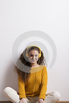 Portrait of a gorgeous teenage girl with curly hair, listening music via headphones. Studio shot, white background with