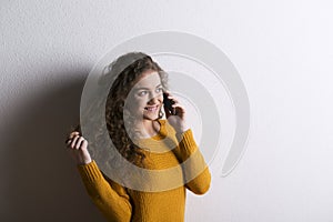 Portrait of a gorgeous teenage girl with curly hair, making phone call. Studio shot, white background with copy space
