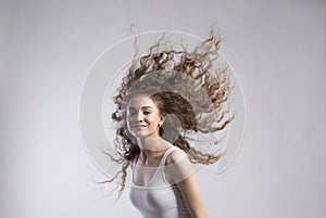 Portrait of a gorgeous teenage girl with flying curly hair, blowing in wind. Studio shot, white background with copy