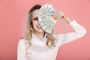 Portrait of gorgeous woman smiling and holding money fan isolated over pink background