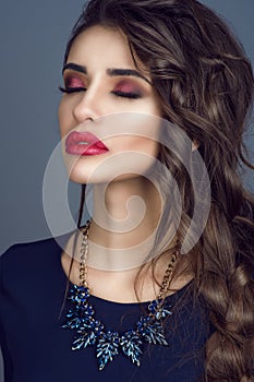 Portrait of gorgeous young lady with perfect skin, red filled lips and long plaited dark hair standing with closed eyes.