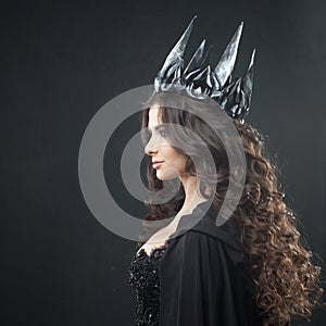 Portrait of a Gothic Princess. Beautiful young brunette woman in metal crown and black cloak.