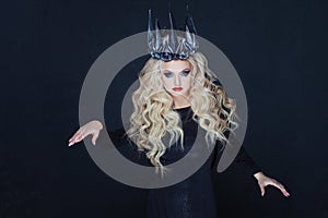 Portrait of a Gothic Queen. Beautiful young blonde woman in metal crown and black cloak.