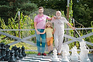 Portrait of grandfather father and son playing chess. Happy men in different ages playing chess board game. Three men