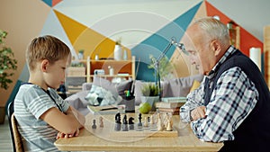 Portrait of grandfather and grandson playing chess moving chessmen on board