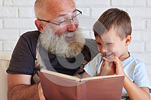 Portrait of grandfather and his small grandson reading a book to