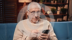 Portrait of grandfather with modern smartphone, old male person using mobile gadget at home and rest