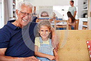 Portrait Of Grandfather Sitting With Granddaughter On Sofa At Home