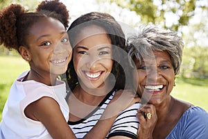 Portrait Of Grandmother With Adult Daughter And Granddaughter Relaxing In Park