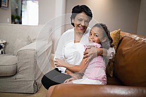 Portrait of grandmother and granddaughter embracing on sofa at home