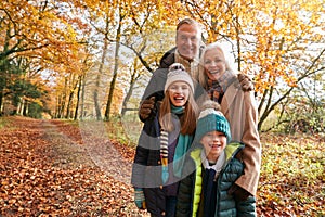 Portrait Of Grandparents With Grandchildren Enjoying Walk Along Autumn Woodland Path Together