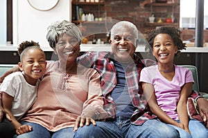 Portrait Of Grandparents Sitting On Sofa At Home With Granddaughters