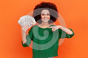 Portrait of gratified rich woman with Afro hairstyle wearing green sweater pointing finger on earned