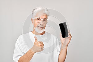 Portrait of gray-haired man in white T-shirt with mobile phone in hand celebrates victory, winning money. Person with smartphone