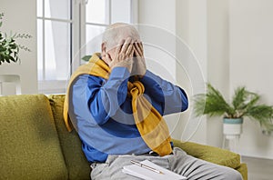 Portrait of gray-haired senior man suffering from headache disease covering face with hands at home