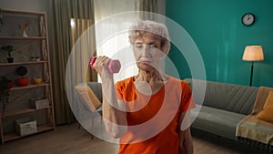 Portrait of a grayhaired elderly woman doing fitness exercises with dumbbells at home close up. A mature woman pumps up