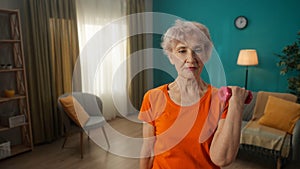 Portrait of a grayhaired elderly woman doing fitness exercises with dumbbells at home close up. A mature woman pumps up