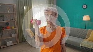 Portrait of a grayhaired elderly woman doing fitness exercises with dumbbells at home close up. A mature woman pumps up