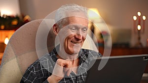 Portrait of grey-haired senior Caucasian man waving talking using video chat on digital tablet on New Year's eve