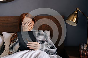 Portrait of grief-stricken young woman lying on bed covering face with hand and crying while holding picture frame