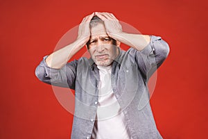 Portrait of a groggy upset worried sad, depressed, tired senior man with a headache, very stressed,  on red background, photo