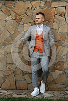 portrait of the groom in a gray suit and an orange vest